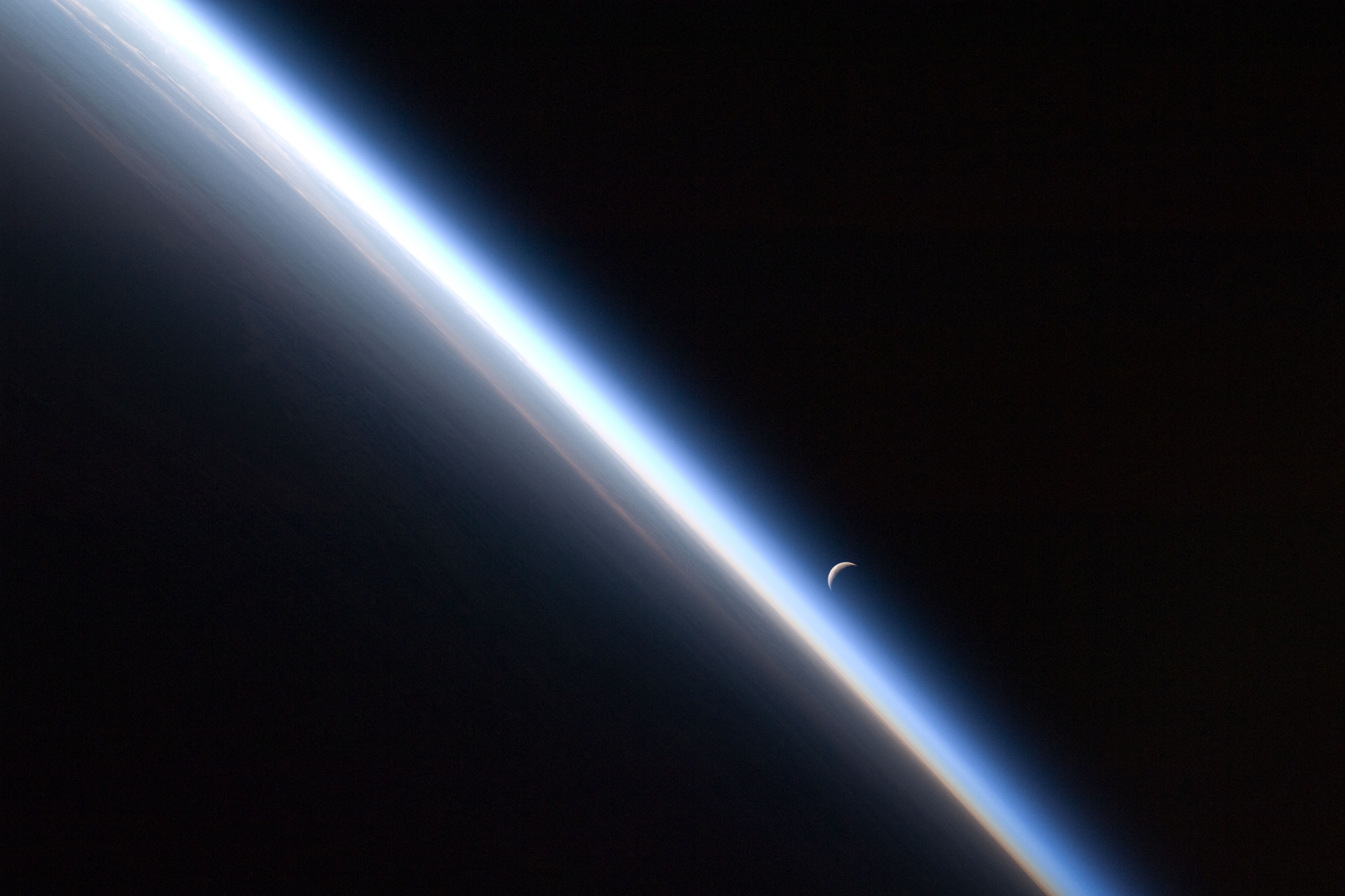 A crescent Moon rises against the edge of Earth